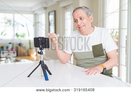 Handsome senior man doing video conference talking to the smartphone camera smiling with happy face looking and pointing to the side with thumb up.