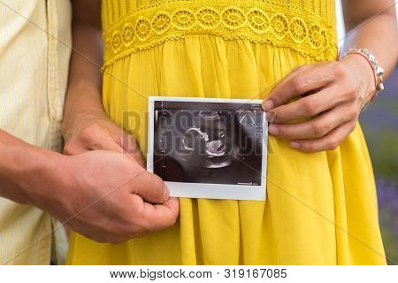 Young Pregnat Couple Holding Black And White Ultrasound Image Of Their Baby In The Lavender Fields W