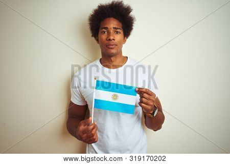 Afro american tourist man holding Argentinian Argentina flag over isolated white background with a confident expression on smart face thinking serious