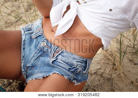 Close-up Chic Fit Sports Girl In White Shirt And Denim Shorts On A Sandy Beach