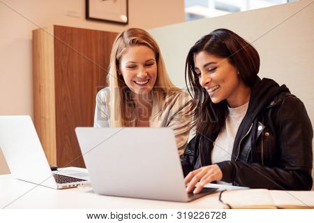 Two Young Businesswomen In Meeting Around Table In Modern Open Plan Workspace