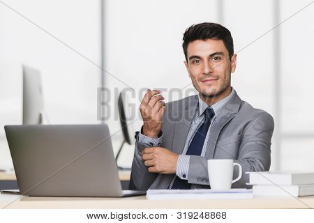 Smiling Handsome Caucasian Businessman Touch His Wrist, There Is Notebook Computer On Table In Moder