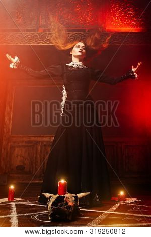 A full length portrait of a scary witch in the wooden house. Magic, dark force, spell. 