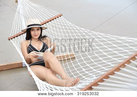 Sexy Asian Woman In Black And White Bikini Who Lying N A Hammock And Reading Book On Sandy Beach Wit