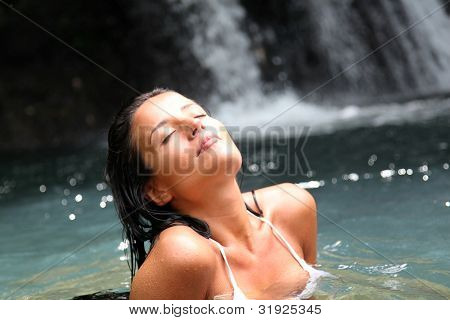 Beautiful woman enjoying bathing near natural waterfall