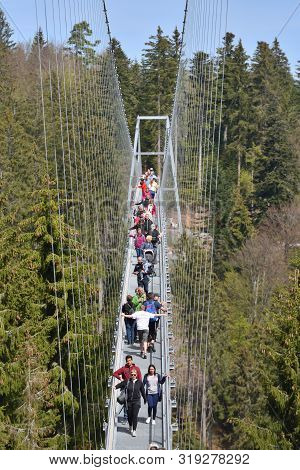 Bad Wildbad, Germany - April 22, 2019: Tourists Walk Along A Long And Suspended Iron Cable Bridge Fo