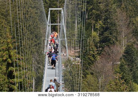 Bad Wildbad, Germany - April 22, 2019: Tourists Walk Along A Long And Suspended Iron Cable Bridge Fo
