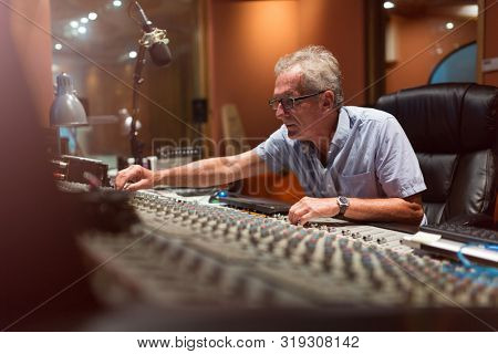Male middle aged recording engineer in a recording studio sitting at a multi channel console