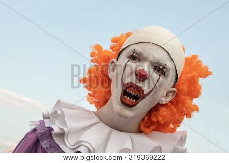 Portrait Of A Guy In The Image Of A Clown With Sharp Teeth On A Background Of Blue Sky. Carnival Cos