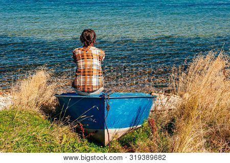 Back View Of A Woman Sitting On Fishing Boat In A Calm Lake Water.