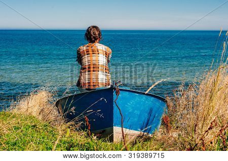 Back View Of A Woman Sitting On Fishing Boat In A Calm Lake Water.