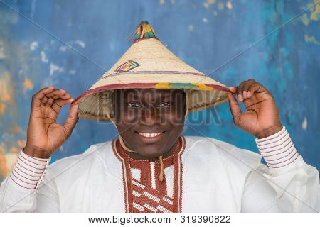 Happy Handsome African Man In Traditional White Dress And Fulani Hat Smiling, Closeup Portrait