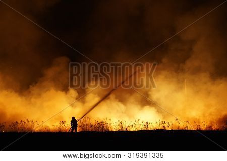 Silhouette Of Fireman Fighting Bushfire At Night, Man Against The Fire.