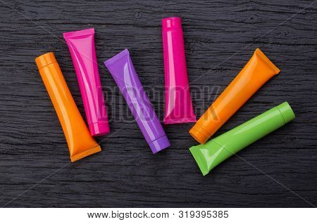 Four Bright Multi-colored 3d Moсkup Tubes For Cosmetics On A Black Wooden Background