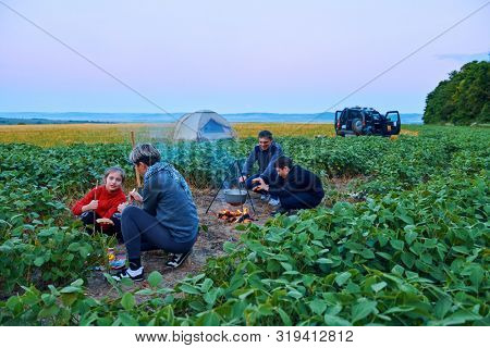 Family traveling and camping, twilight, cooking on the fire. Beautiful nature - field, forest and moon.