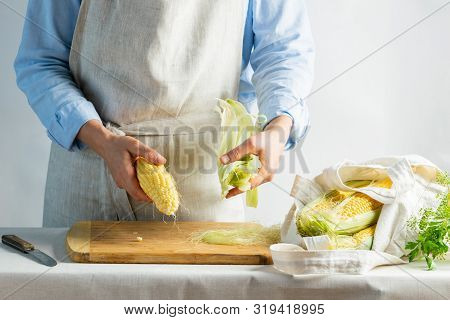 A Female Cook A Cotton Apron Cleans Ripe Corn On The Cob. Rustic Natural Style. The Concept Organic 