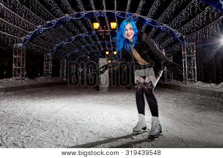 Girl With Blut Hair Skating On The Ice Arena In The Evening City Square In Winter