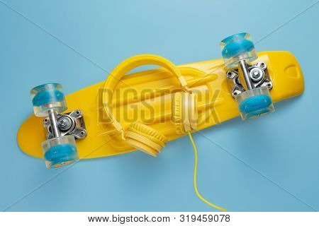 Yellow Headphones And Skateboard Or Pennyboard On Blue Background. Music Concept.