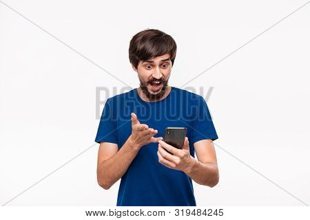 Good Looking Brunet Man In A Blue Shirt With Beard And Mostaches Surprised Looking At The Screen Of 