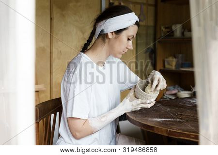 Beautiful Woman In A Creative Workshop Sits At A Table And Wipes A Clay Bowl