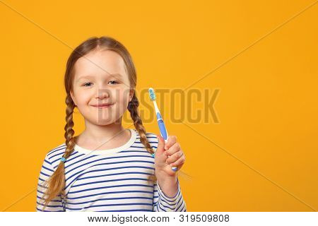 A Little Child Girl In A Striped Pajamas Holding A Toothbrush. The Concept Of Daily Hygiene. Yellow 