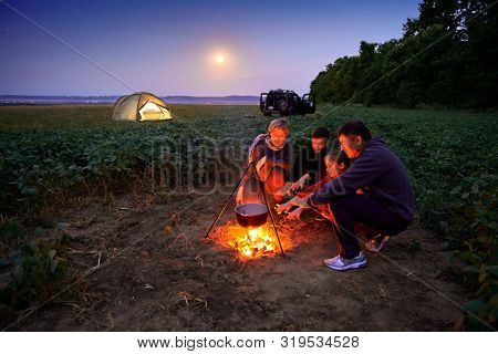 Family traveling and camping, twilight, cooking on the fire. Beautiful nature - field, forest, stars and moon.