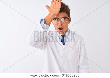 Young handsome sciencist man wearing glasses and coat over isolated white background surprised with hand on head for mistake, remember error. Forgot, bad memory concept.