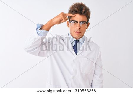 Young handsome sciencist man wearing glasses and coat over isolated white background pointing unhappy to pimple on forehead, ugly infection of blackhead. Acne and skin problem