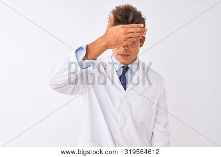 Young handsome sciencist man wearing glasses and coat over isolated white background covering eyes with hand, looking serious and sad. Sightless, hiding and rejection concept