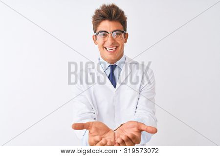 Young handsome sciencist man wearing glasses and coat over isolated white background Smiling with hands palms together receiving or giving gesture. Hold and protection