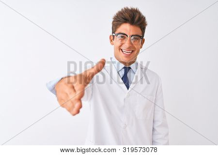 Young handsome sciencist man wearing glasses and coat over isolated white background smiling friendly offering handshake as greeting and welcoming. Successful business.
