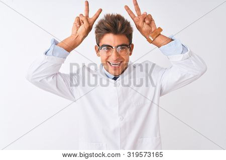 Young handsome sciencist man wearing glasses and coat over isolated white background Posing funny and crazy with fingers on head as bunny ears, smiling cheerful