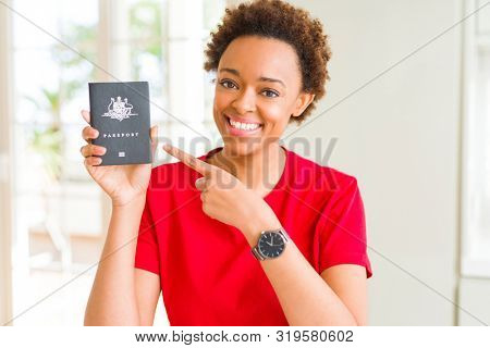 Young african american woman holding Australian passport very happy pointing with hand and finger