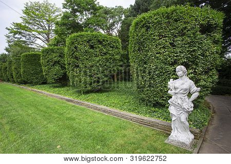 Formal Garden With Trimmed Hedge And A Marble Statue Of Woman