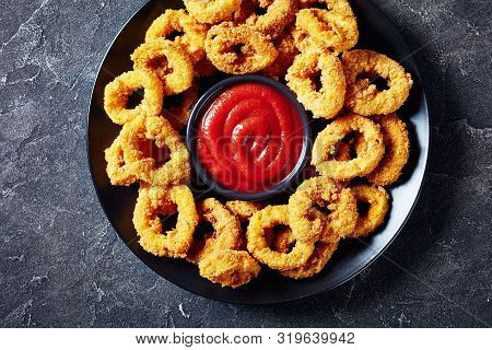 Crispy Calamari Rings, Deep Fried Breaded Squid Rings Served With Tomato Sauce On A Black Plate On A