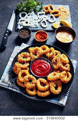 Crispy Calamari Rings, Deep Fried Breaded Squid Rings Served With Tomato Sauce On A Black Plate On A