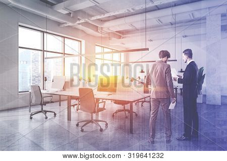 Two Young Businessmen Discussing Work In Modern Open Space Office Corner In Industrial Style With Wh