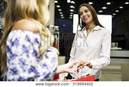 Polite Smiling Saleswoman Passes Packed Trendy Purchases To A Blonde Customer