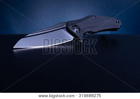 Sharp Knife With A Black Handle And A Black Blade. Blue Background.