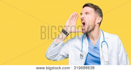 Handsome doctor man wearing medical uniform over isolated background shouting and screaming loud to side with hand on mouth. Communication concept.