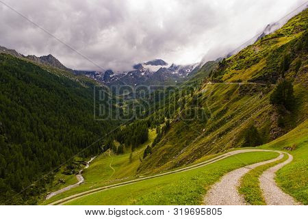 Photo Of Passo Rombo On A Gloomy Day In August With River Meadows, Pines, Pebbles And Breathtaking V