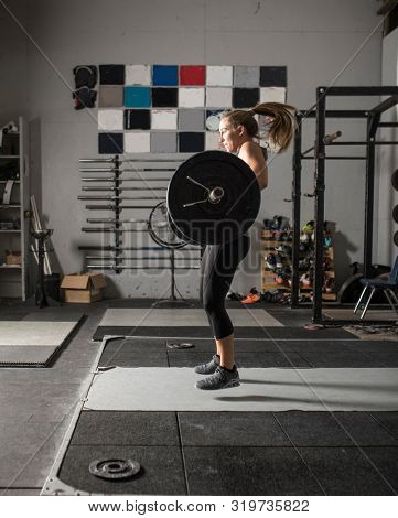 Action shot of female power lifter doing clean and jerk with heavy weights in gym.
