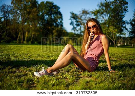 Vape Teenager. Young Pretty Sporty Caucasian Girl In A Pink Jumpsuit And Sunglasses Smoking An Elect