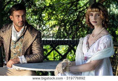 Handsome Young Couple In Vintage Clothing Sit In Gazebo. The Female Is Looks At Camera As Her Compan