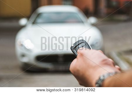 The Man Opens The Car With A Keychain, In The Background Is A White Car