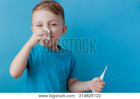 Ill Young Child With A Thermomether, Measuring The Height Of His Fever And Looking Into The Camera