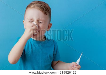 Ill Young Child With A Thermomether, Measuring The Height Of His Fever And Looking Into The Camera