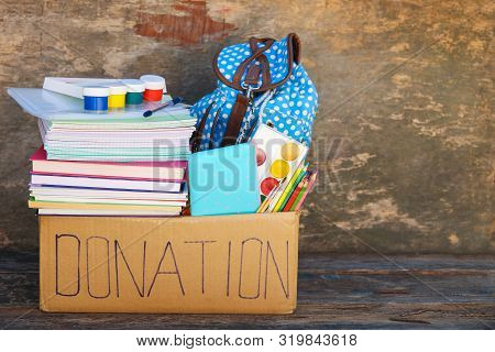 Donation Box With School Supplies On Old Wooden Background.
