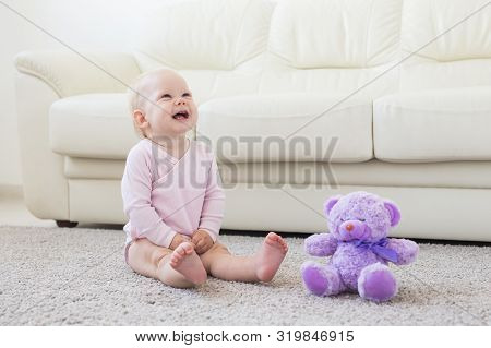 Childhood, Babyhood And Children Concept - Happy Little Baby Girl Sitting On Floor At Home