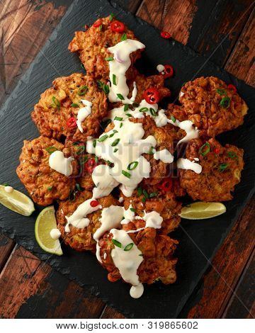 Indian Takeaway Food, Spicy Onion Bhajis Served With Chili Yoghurt Dip And Lime Wedges On Wooden Boa